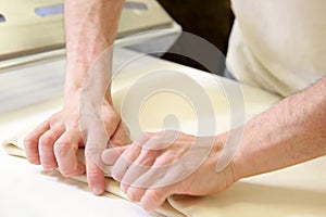 Rolling out dough by male hands at bakery