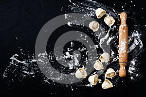 Rolling pin and raw dumplings with flour on dark black baking background, top view, copy space for text, menu, recipe.