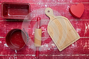 Rolling pins, cookie cutters, and flour on a red wooden background. Heart and cutting board. View from above. Space for text