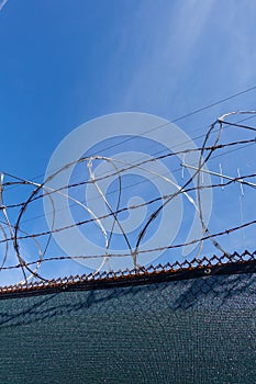 Rolls of barbed wire and razor wire on top of a chain link fence with a deep blue sky background