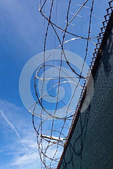 Rolls of barbed wire and razor wire on top of a chain link fence with a deep blue sky background