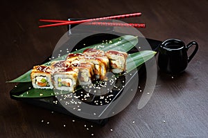 Rolls with eel and cheese on the board with sauce and red chopsticks