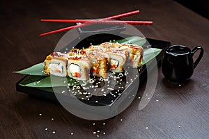 Rolls with eel and cheese on the board with sauce and red chopsticks