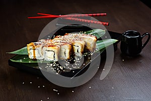 Rolls with eel and cheese on the board with sauce and red chopsticks