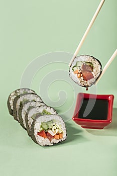 Rolls with fresh vegetables with chopsticks with a plate for soy sauce on a bright green background, side view with a copy space