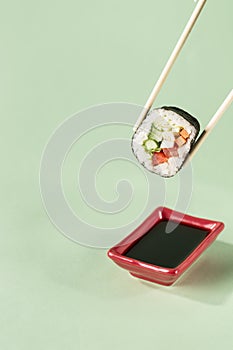 Rolls with fresh vegetables with chopsticks with a plate for soy sauce on a bright green background, side view with a copy space