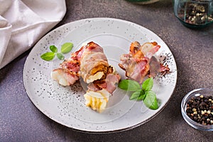Rolls of fried bacon and mashed potatoes and basil on a plate on the table