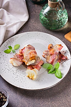 Rolls of fried bacon and mashed potatoes and basil on a plate on the table. Vertical view