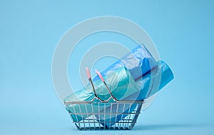 Rolls of plastic bags in a miniature shopping basket on a blue background