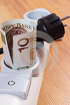 Rolls of polish currency money in electrical power strip and disconnected plug, energy costs