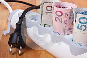 Rolls of polish currency money in electrical power strip and disconnected plug, energy costs