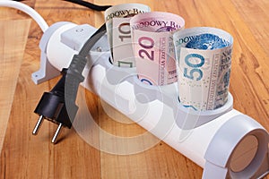 Rolls of polish currency money in electrical power strip and disconnected plug, energy costs