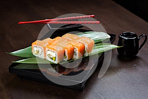 Rolls with salmon, avocado and cheese on the board with sauce and red chopsticks