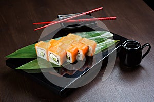 Rolls with salmon and cheese on the board with sauce and red chopsticks