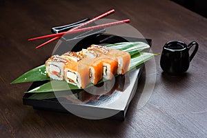 Rolls with salmon, eel and cheese on the board with sauce and red chopsticks