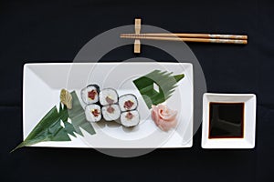 Rolls of sushi with rice nori seeweed and fish on a white plate with hashi chopsticks