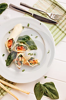 Rolls of thin pancakes with smoked salmon, horseradish cream cheese and spinach leaves. Side view with copy space