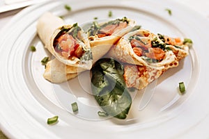 Rolls of thin pancakes with smoked salmon, horseradish cream cheese and spinach leaves. Side view with copy space