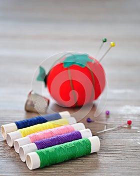 Rolls of thread with an out of focus pin cushion shaped as a red tomato and a thimble