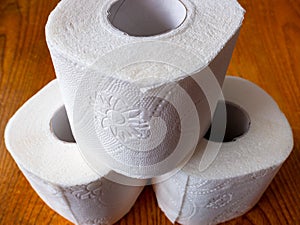 3 rolls of toilet paper stands in the shape of a pyramid on a brown wooden table