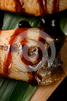 Rolls wrapped in salmon slices drizzled with sauce on a banana leaf close up