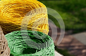 Rolls of yellow and green raffia close-up. Skeins of multi-colored raffia against the background of a green street