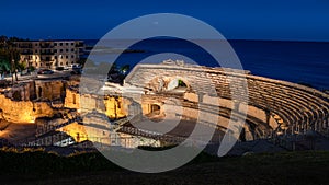 Roman amphitheater illuminated at night. Well-preserved monument in the old city of Tarraco. Inside it there is a Romanesque style photo