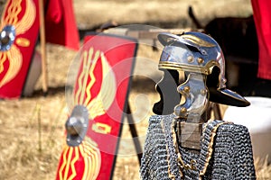 Roman Helmet with chain mail placed on a wood strut with a traditional rectangular shield unfocused in the background