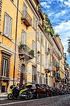 Roman street with beautiful colored houses. A lot of cars are parked under the houses along the road.