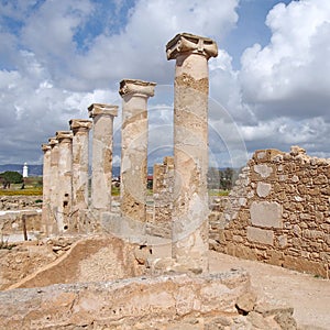 Roman walls and columns in the house of theseus in paphos cyprus with the historic lighthouse in the distance