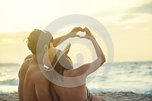 Romance couple made a heart shape together by hands on the beach at sunset. Love, wedding and valentine concept