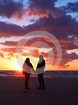 Romance after dark. Silhouette of a couple going for a walk on the beach at sunset.