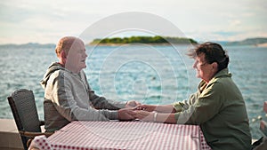romance of elderly spouses, happy old man holding hand of mature wife while relaxing on promenade by the sea