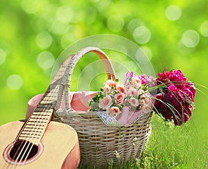 Romance, love, valentine`s day concept - wicker basket with bouquet of flowers, guitar on the grass