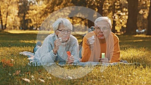 Romance at old age. Elderly couple blowing soap bubbles in the park in autumn