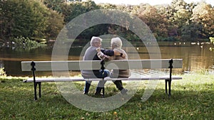 Romance at old age. Elderly couple enjoying autumn day sitting on the bench near the river