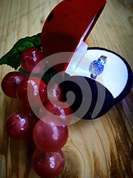Romance: a ring with a blue stone in a box & x22;ladybug& x22; and a pile of grapes on a wooden background