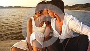 Romance scene of heterosexual mixed race couple of lovers kissing with passion on a wooden pier at sunset - Romantic handsome