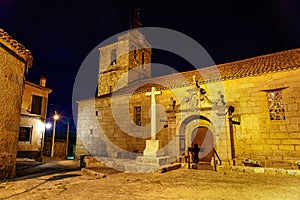 Romanesque church at night with bell tower and stone cross.