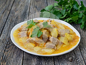 Romanian cuisine - fresh homemade meat and potatoes with parsley. Stew with pork and vegetables on a wooden background