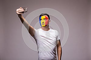 Romanian football fan take selfie photo with phone on grey background.