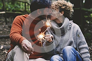 Romantic adult couple kissing in love holding fire sparklers sitting in the nature park enjoy outdoor relationship and leisure