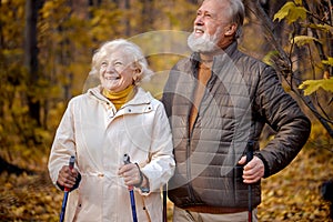 Romantic aged couple enjoying the moment of love in park, nordic walking at autumn day