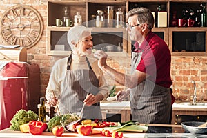 Romantic aged couple tasting food while cooking lunch in kitchen together