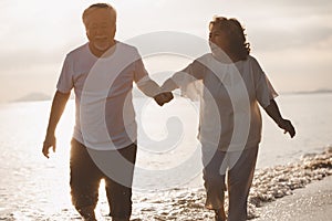 The romantic Asian senior couple hand in hand while walking on summer beach sunset. Travel leisure and activity after retirement