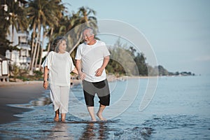 The romantic Asian senior couple hand in hand while walking on summer beach sunset. Travel leisure and activity after retirement