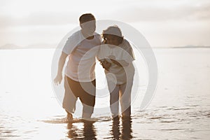 The romantic Asian senior couple hand in hand while walking on summer beach sunset. Travel leisure and activity after retirement