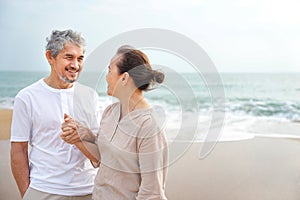 romantic asian senior couple standing at the beach,smiling,looking at each other and hands holding together
