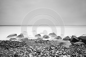 Romantic atmosphere in peaceful morning at sea. Big boulders sticking out from smooth wavy sea. Pink horizon