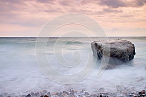 Romantic atmosphere in peaceful morning at sea. Big boulders sticking out from smooth wavy sea. Pink horizon